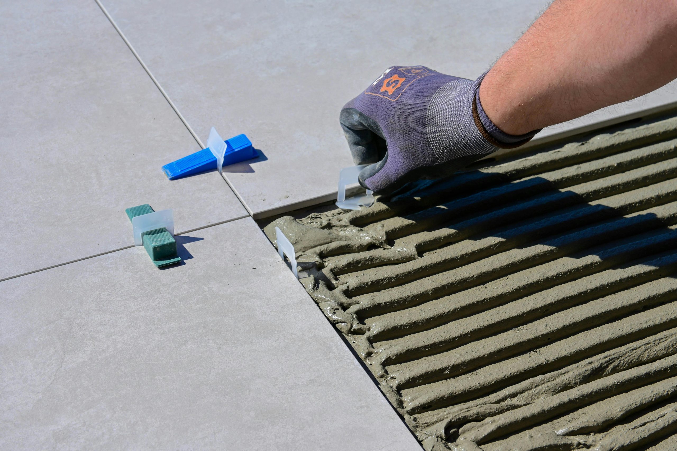 Vue détaillée d'une main gantée alignant des carreaux avec des nivelleurs et des croisillons lors d'une construction.