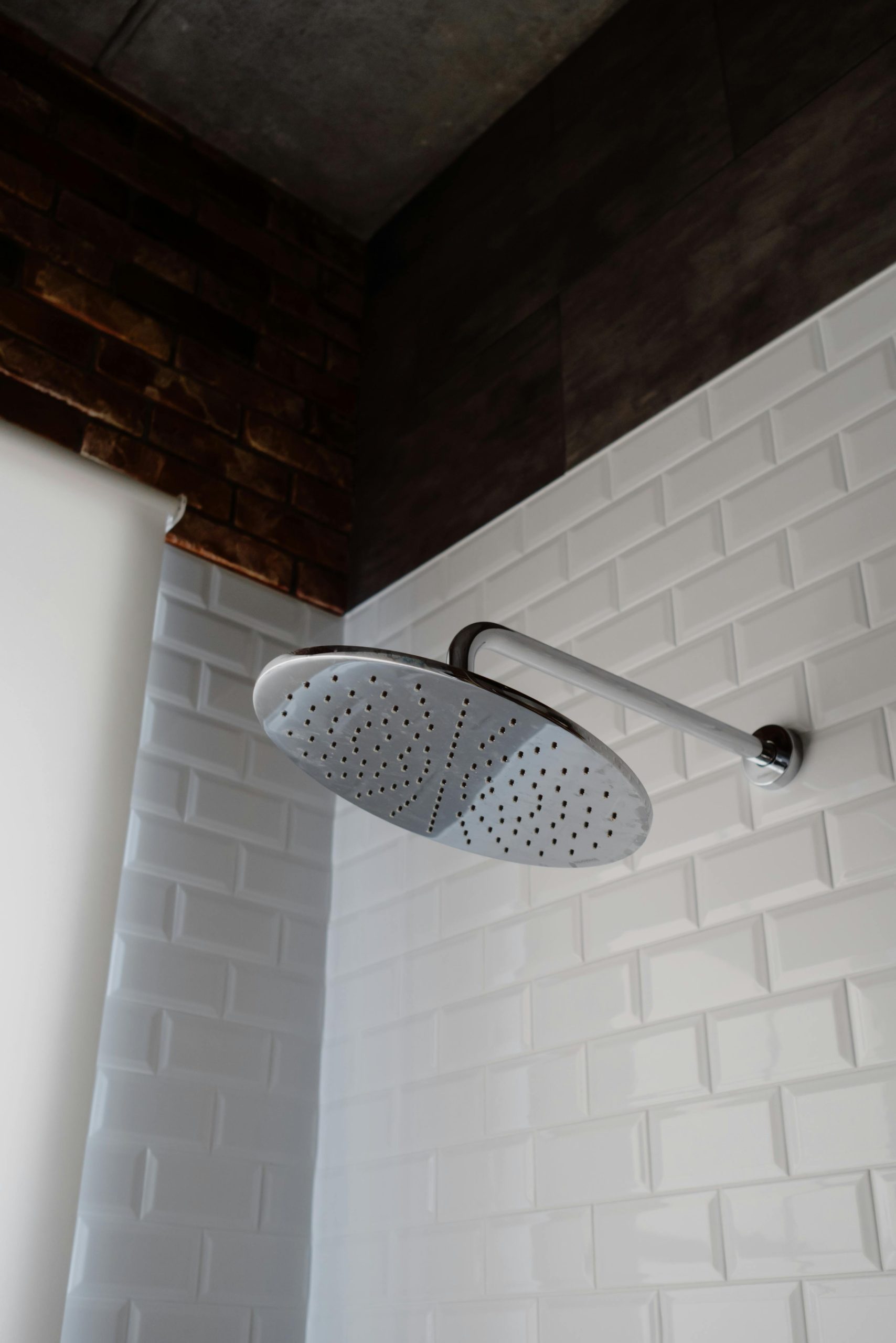Robinet de douche en acier inoxydable élégant sur fond de salle de bain stylisée avec carrelage blanc et mur d'accent en brique.