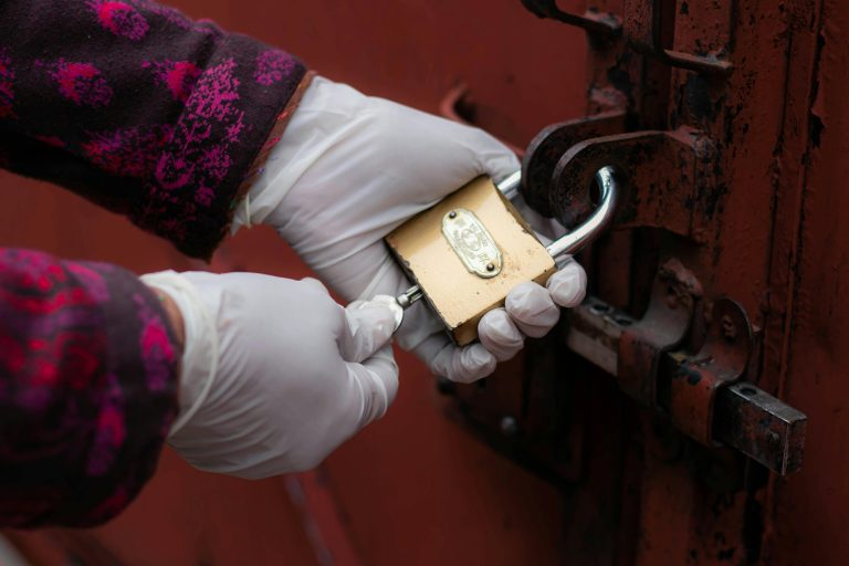 Un gros plan de mains gantées déverrouillant un cadenas de porte rouillé.