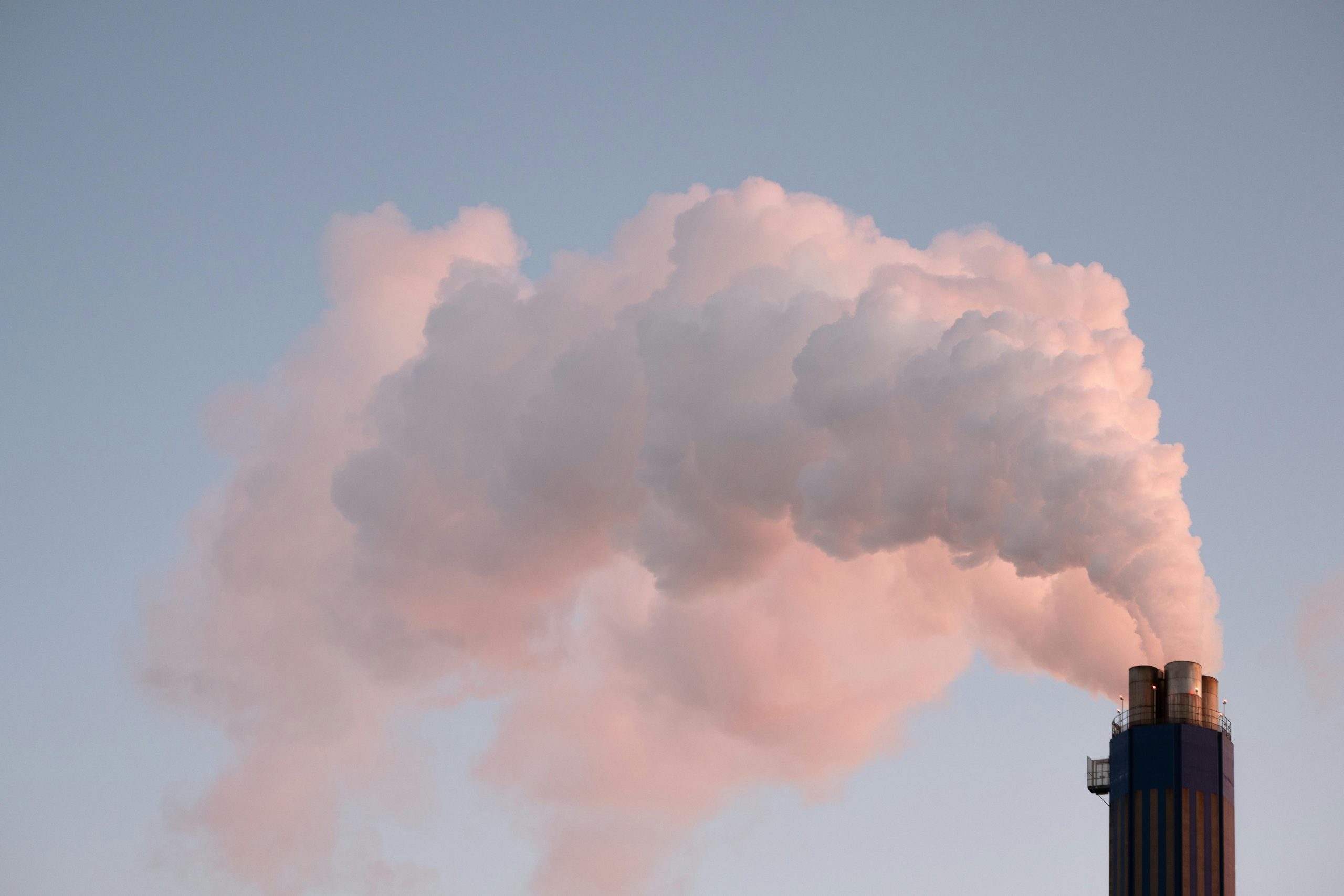 From below of clouds of smoke from industrial factory pipes polluting atmosphere against cloudless sky Des nuages de fumée provenant des cheminées d'une usine industrielle polluant l'atmosphère sur un ciel sans nuages vu d'en bas