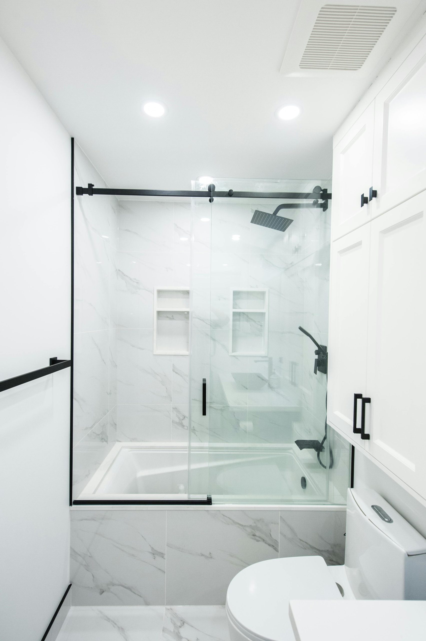 Salle de bain moderne et élégante avec des carreaux de marbre blanc, des portes de douche en verre et des accents noirs.