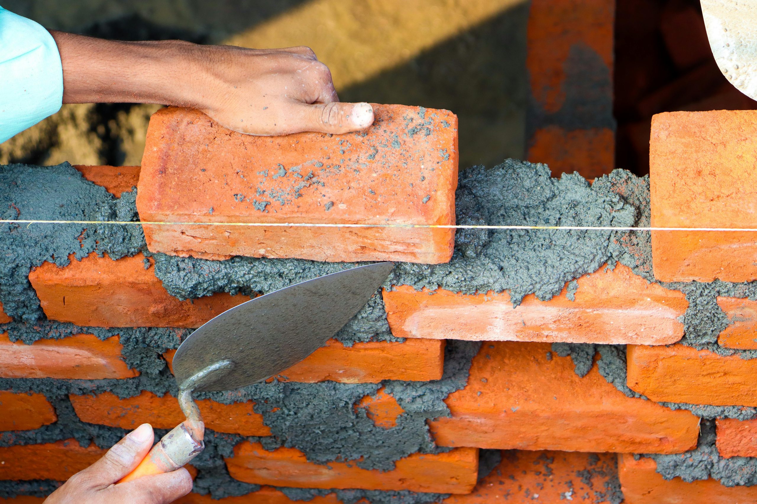 Mains posant des briques avec du ciment dans un cadre de construction, illustrant un travail de maçonnerie précis.