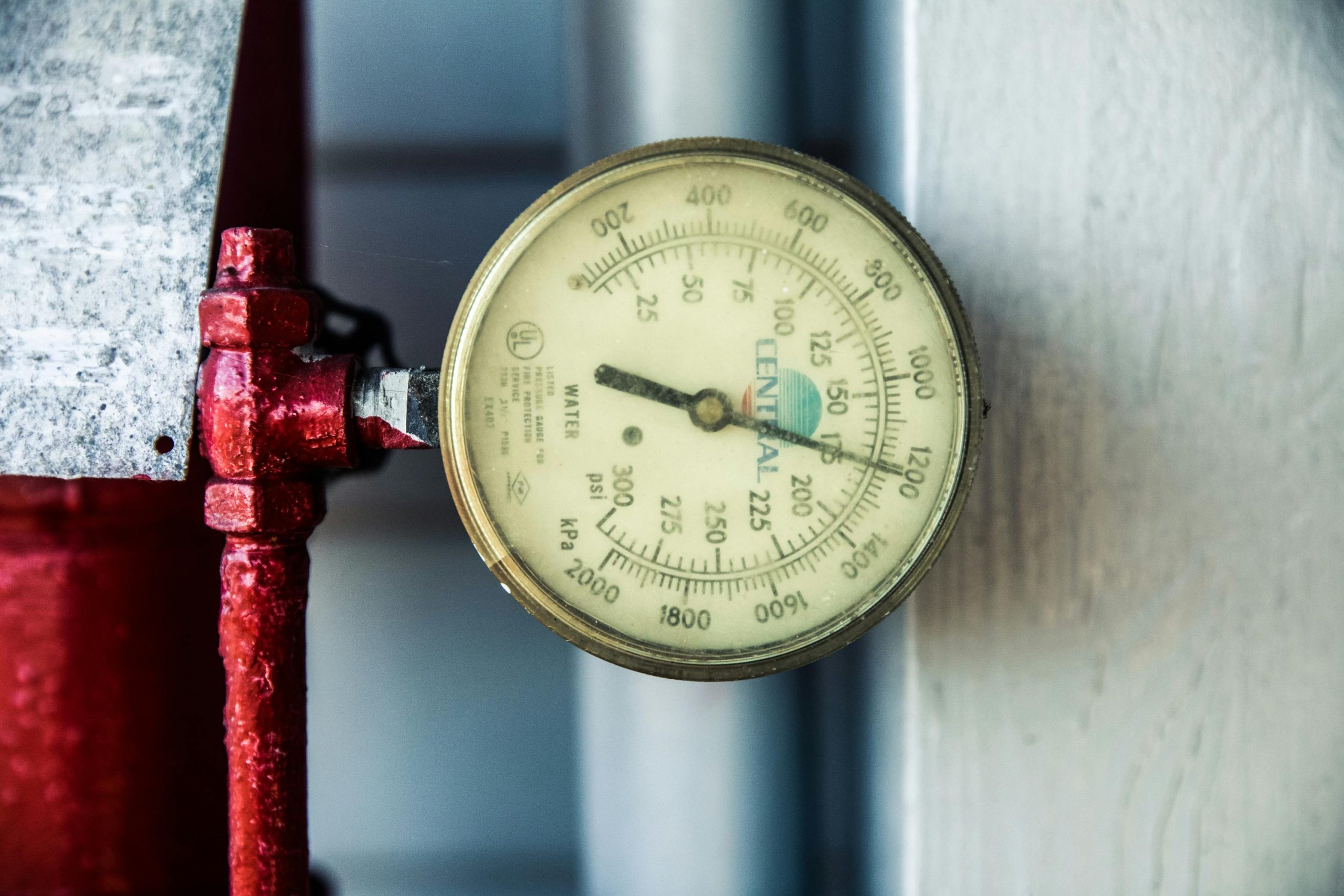 Détail d'un manomètre fixé à un tuyau industriel rouge, mesurant les PSI et kPa.