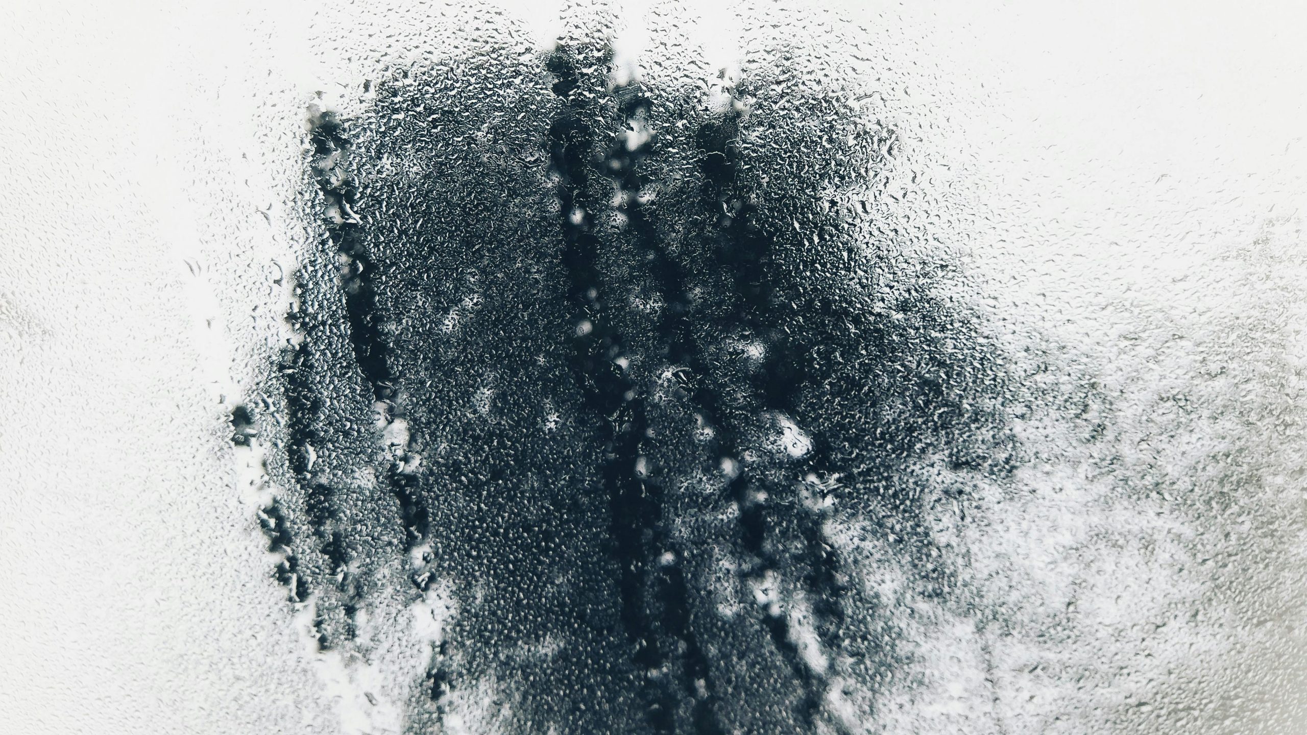 Detailed image of water droplets forming patterns on a glass window, evoking a cold atmosphere. Image détaillée de gouttes d'eau formant des motifs sur une vitre, évoquant une atmosphère froide.