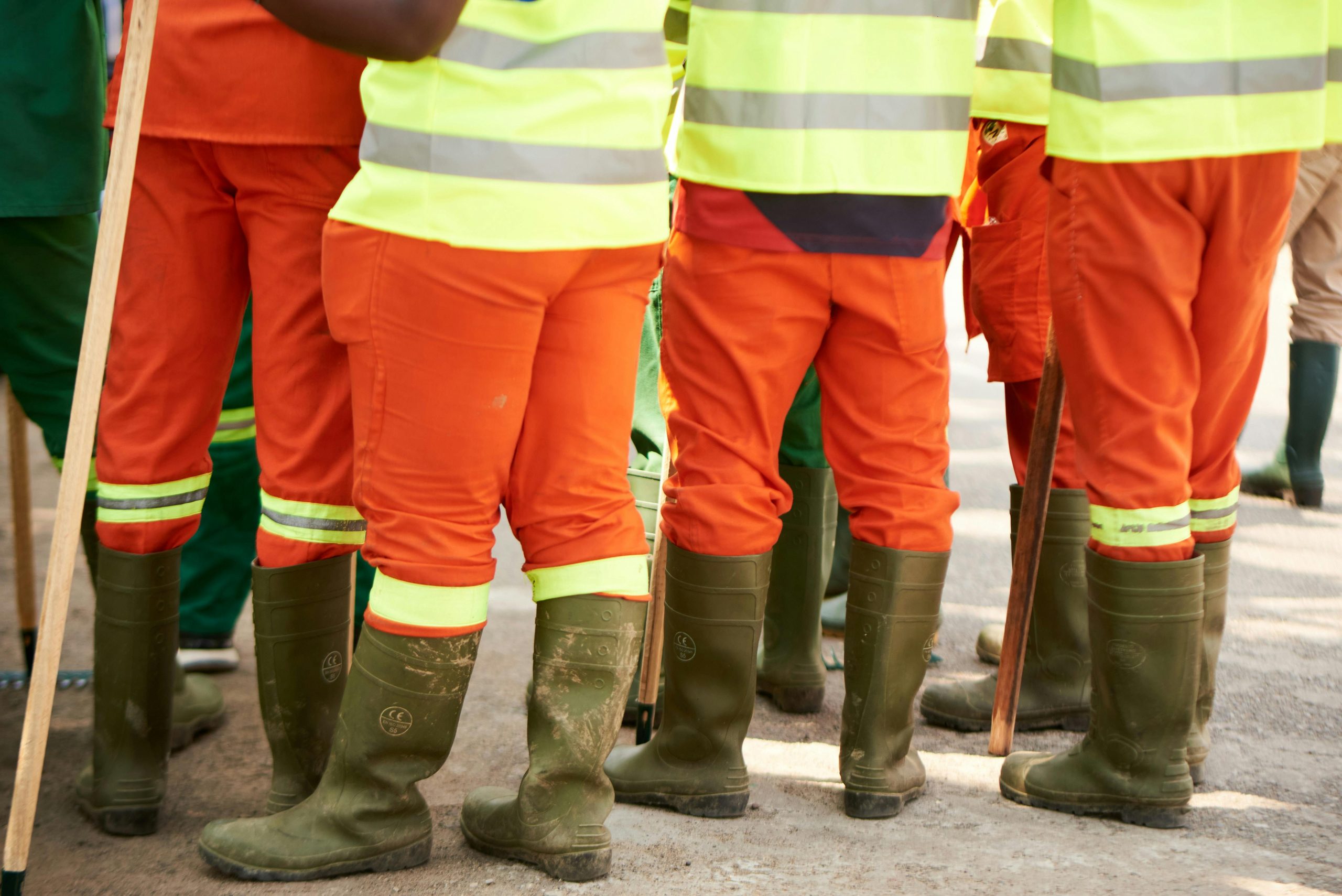 Group of construction workers wearing high visibility gear and boots standing outdoors. Groupe de travailleurs de la construction portant des vêtements de haute visibilité et des bottes debout à l'extérieur.