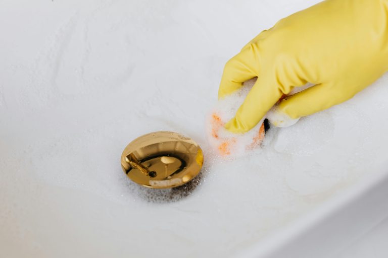 From above of crop anonymous person in yellow rubber protective glove using sponge and detergent for washing white sink in bathroom Vue de dessus d'une personne anonyme recadrée portant un gant de protection en caoutchouc jaune utilisant une éponge et un détergent pour laver un lavabo blanc dans une salle de bain