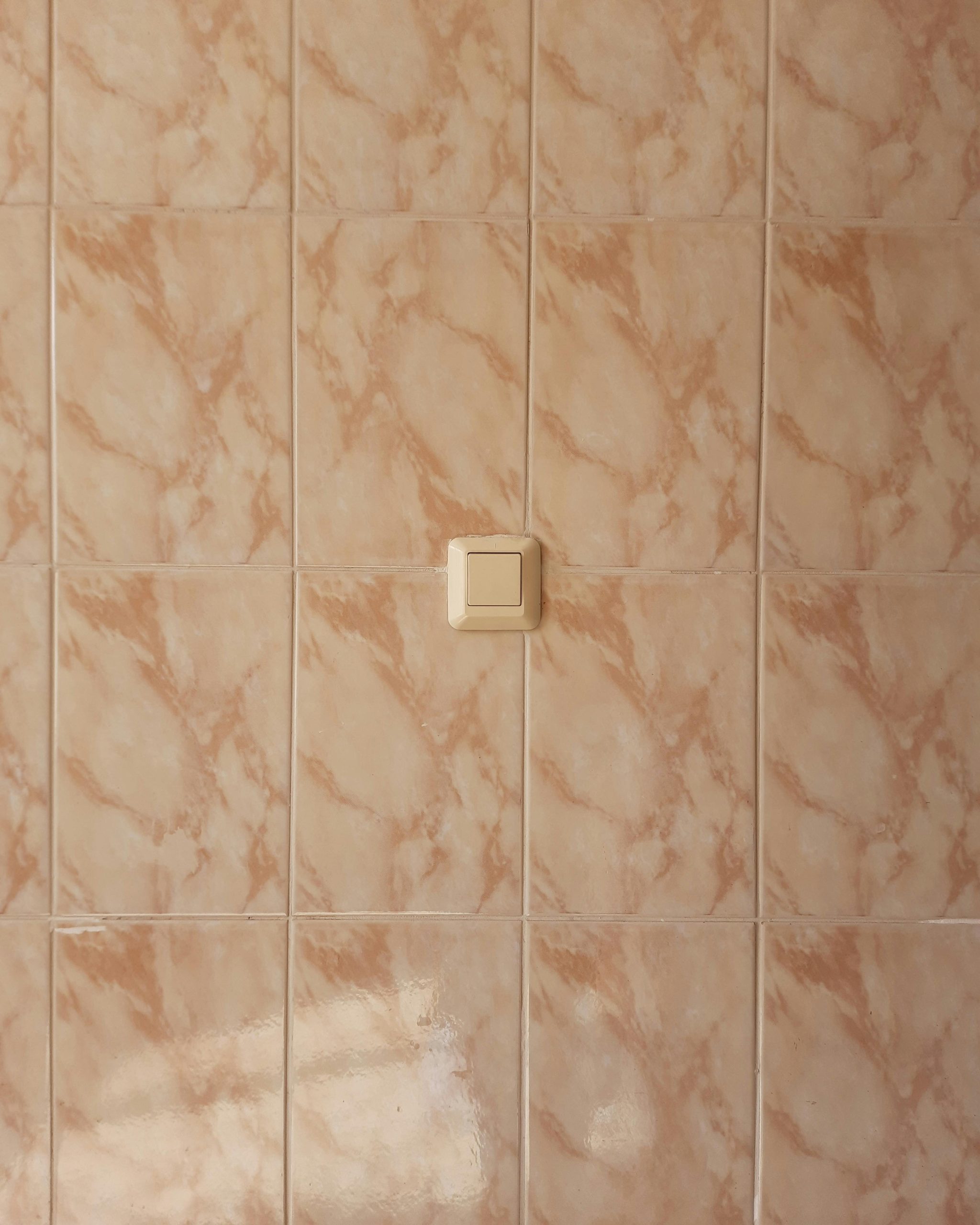 Aesthetic beige ceramic tiles wall featuring a centered single light switch, offering a clean and minimalistic appearance. Mur de carreaux en céramique beige esthétique présentant un interrupteur unique centré, offrant une apparence propre et minimaliste.