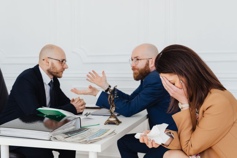A lawyer mediates an emotional settlement discussion with a distressed couple in a legal office. Un avocat préside à une discussion de règlement chargée d'émotions avec un couple en détresse dans un bureau juridique.