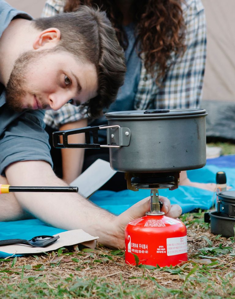 Calm hiker lighting camping stove while preparing food in pan with girlfriend in nature in daytime Randonneur calme allumant un réchaud de camping tout en préparant de la nourriture dans une poêle avec sa petite amie dans la nature en plein jour
