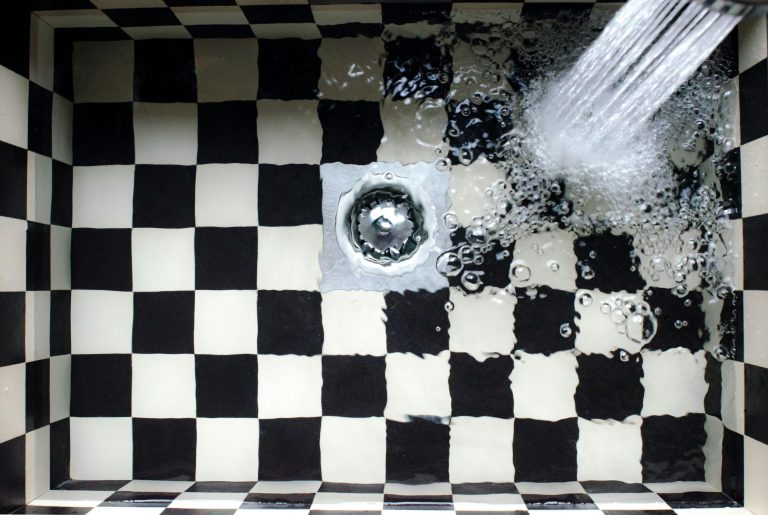 Top view of a checkered sink with water splashing, showcasing elegant design. Vue de dessus d'un lavabo à carreaux avec de l'eau qui éclabosse, mettant en avant un design élégant.