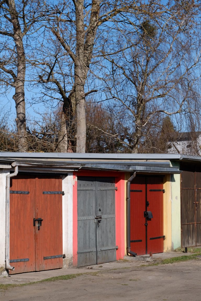 Vibrant red, gray, and yellow garage doors in a quiet outdoor area with trees. Des portes de garage rouge vif, gris et jaune dans un endroit extérieur calme avec des arbres.