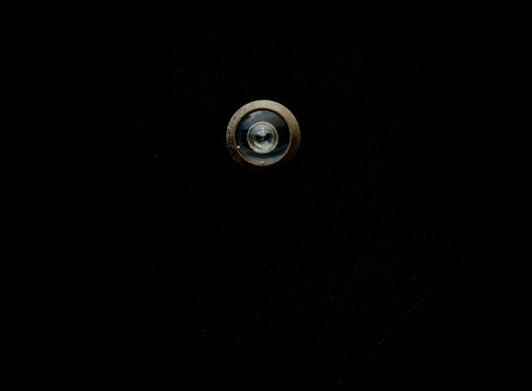 Close-up image of a metallic door peephole with a black background, offering copy space. Gros plan d'un judas de porte métallique sur fond noir, offrant de l'espace pour le texte.