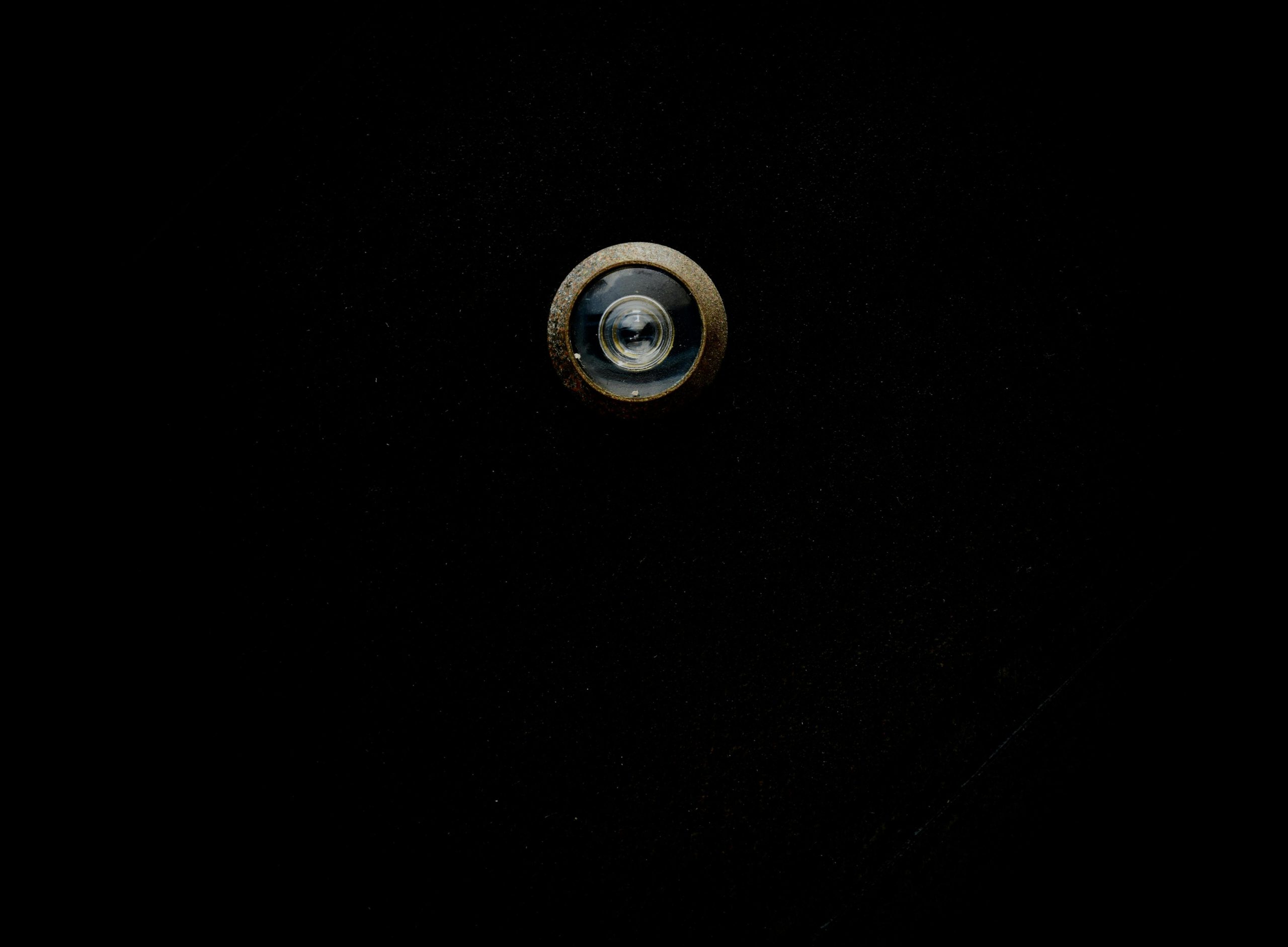 Close-up image of a metallic door peephole with a black background, offering copy space. Gros plan d'un judas de porte métallique sur fond noir, offrant de l'espace pour le texte.