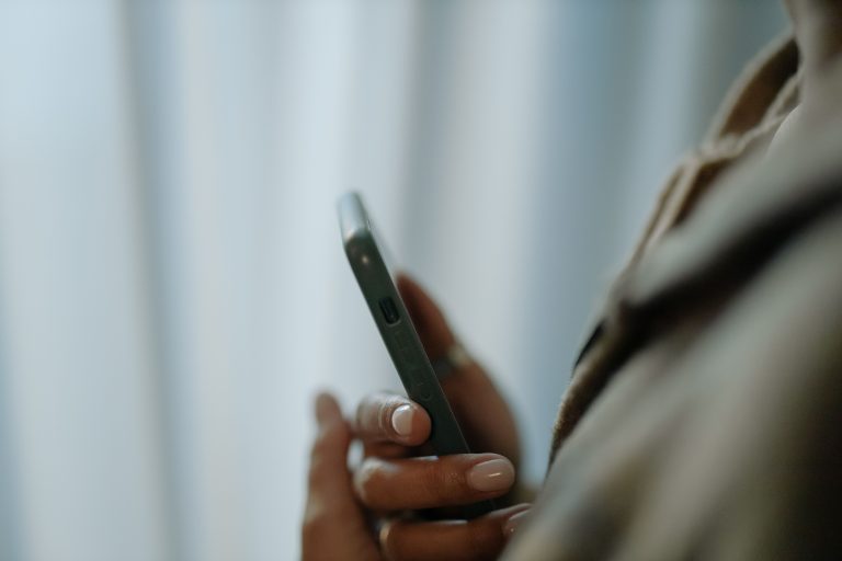 A focused close-up of a female hand holding a smartphone indoors with a soft background. Gros plan concentré d'une main féminine tenant un smartphone à l'intérieur avec un arrière-plan doux.