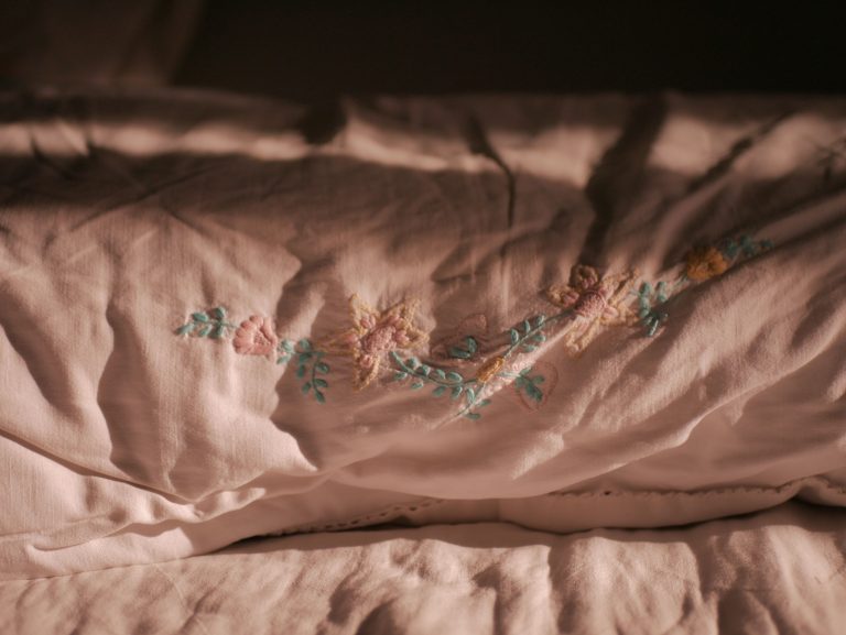 Close-up of delicate floral embroidery on a soft pink pillowcase, showcasing elegance. Gros plan sur une broderie florale délicate sur une taie d'oreiller rose pâle, mettant en évidence l'élégance.
