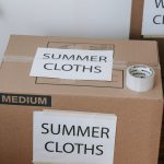 Labeled cardboard boxes for summer clothes ready for moving or storage, with packing tape and labels. Boîtes en carton étiquetées pour vêtements d'été prêtes pour un déménagement ou un stockage, avec du ruban adhésif et des étiquettes.