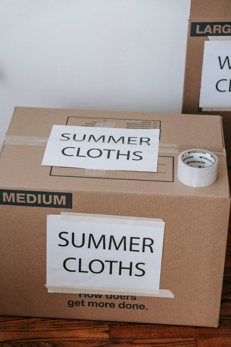 Labeled cardboard boxes for summer clothes ready for moving or storage, with packing tape and labels. Boîtes en carton étiquetées pour vêtements d'été prêtes pour un déménagement ou un stockage, avec du ruban adhésif et des étiquettes.