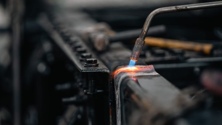 Detailed view of torch welding metal surface, featuring blue flame. Vue détaillée de la surface métallique soudée à la torche, avec une flamme bleue.
