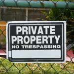 Close-up of a private property no trespassing sign on a chain-link fence with greenery in the background. Gros plan d'un panneau « Propriété privée, interdiction d'entrer » sur une clôture à mailles losangées avec de la verdure en arrière-plan.