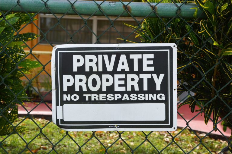 Close-up of a private property no trespassing sign on a chain-link fence with greenery in the background. Gros plan d'un panneau « Propriété privée, interdiction d'entrer » sur une clôture à mailles losangées avec de la verdure en arrière-plan.