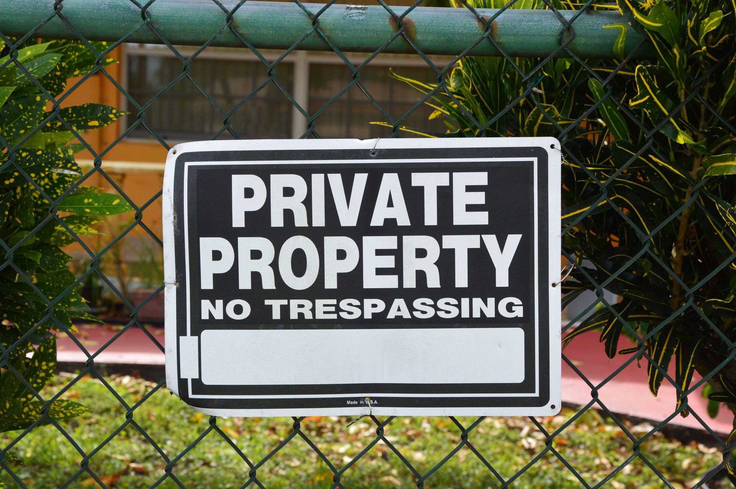 Close-up of a private property no trespassing sign on a chain-link fence with greenery in the background. Gros plan d'un panneau « Propriété privée, interdiction d'entrer » sur une clôture à mailles losangées avec de la verdure en arrière-plan.