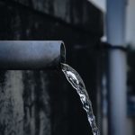 Close-up view of water pouring from an industrial metal pipe, captured outdoors. Vue rapprochée de l'eau versée d'un tuyau métallique industriel, capturée en extérieur.