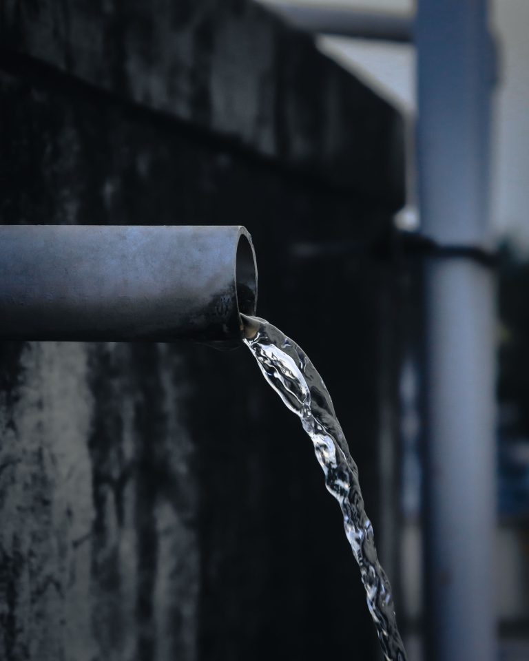 Close-up view of water pouring from an industrial metal pipe, captured outdoors. Vue rapprochée de l'eau versée d'un tuyau métallique industriel, capturée en extérieur.