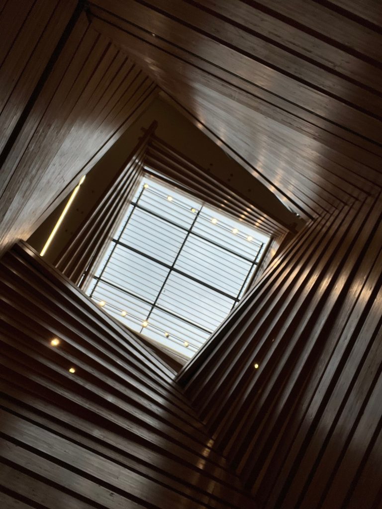Plafond en bois géométrique complexe avec panneau de lumière naturelle, offrant une perspective architecturale moderne.