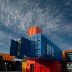 Vibrant shipping containers arranged creatively under a bright sky, showcasing modern architectural innovation. Conteneurs d'expédition vibrants arrangés de manière créative sous un ciel lumineux, mettant en avant l'innovation architecturale moderne.