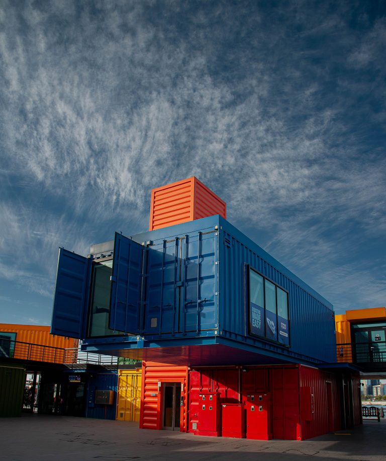 Vibrant shipping containers arranged creatively under a bright sky, showcasing modern architectural innovation. Conteneurs d'expédition vibrants arrangés de manière créative sous un ciel lumineux, mettant en avant l'innovation architecturale moderne.
