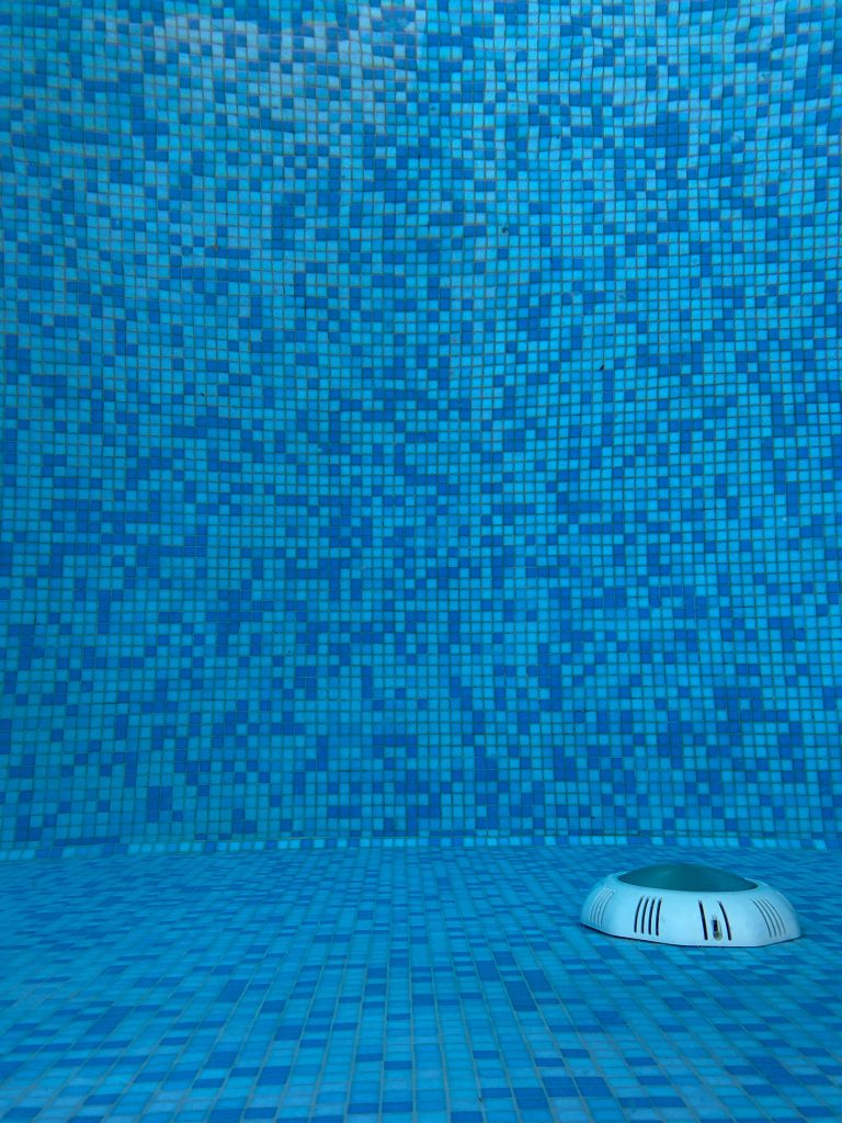 Vibrant blue mosaic tiles in a swimming pool with a visible drain. Carrelage mosaïque bleu vibrant dans une piscine avec un drain visible.