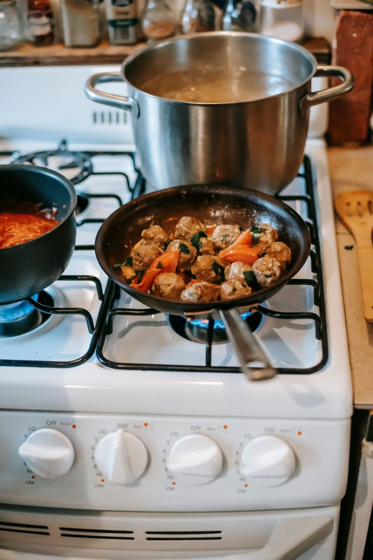 From above of appetizing meatballs in frying pan placed on gas stove near saucepans with boiling dishes in kitchen Vue de dessus de boulettes de viande appétissantes dans une poêle à frire placée sur un réchaud à gaz près de casseroles avec des plats bouillants dans la cuisine
