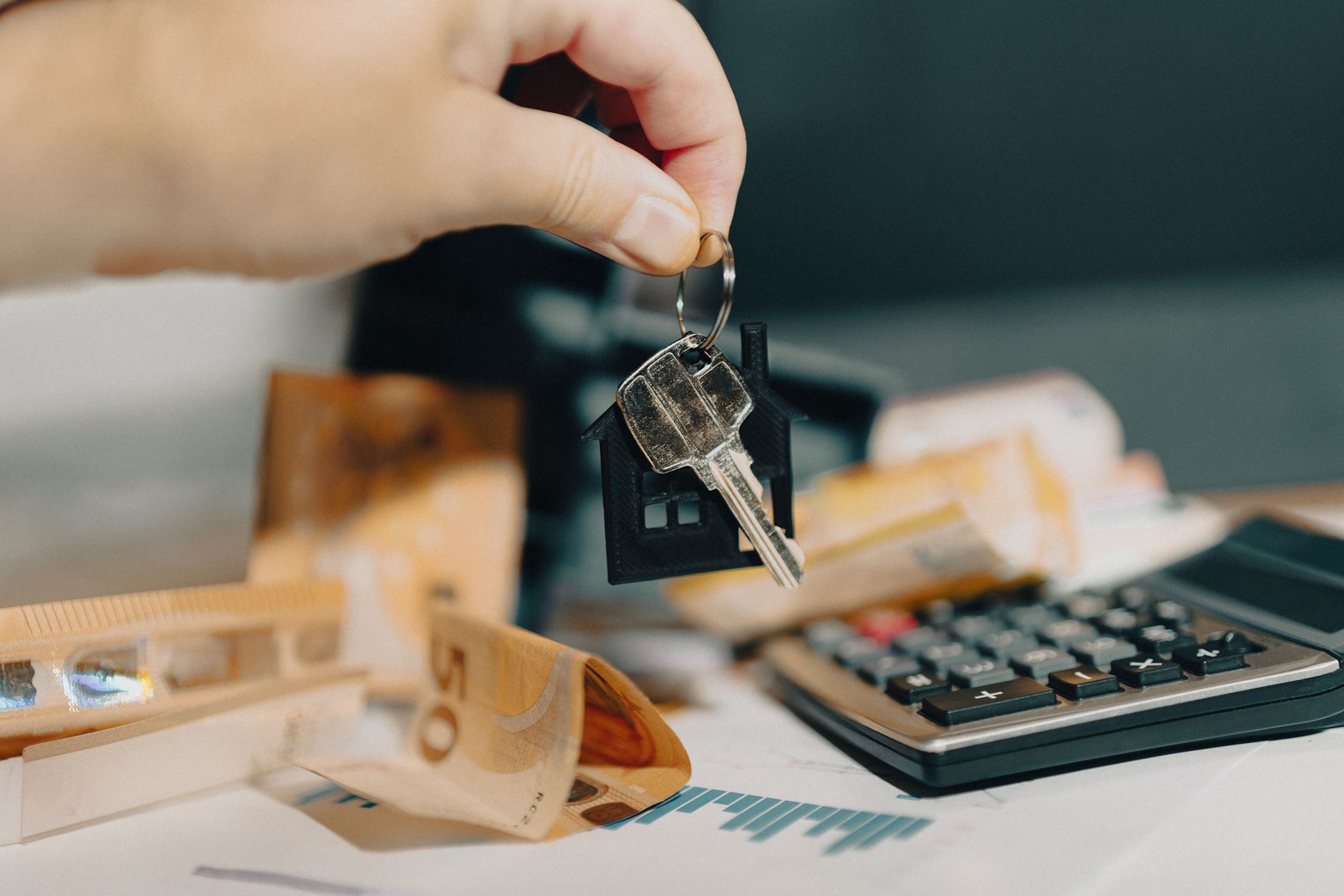 Main tenant des clés au-dessus de billets et d’une calculatrice